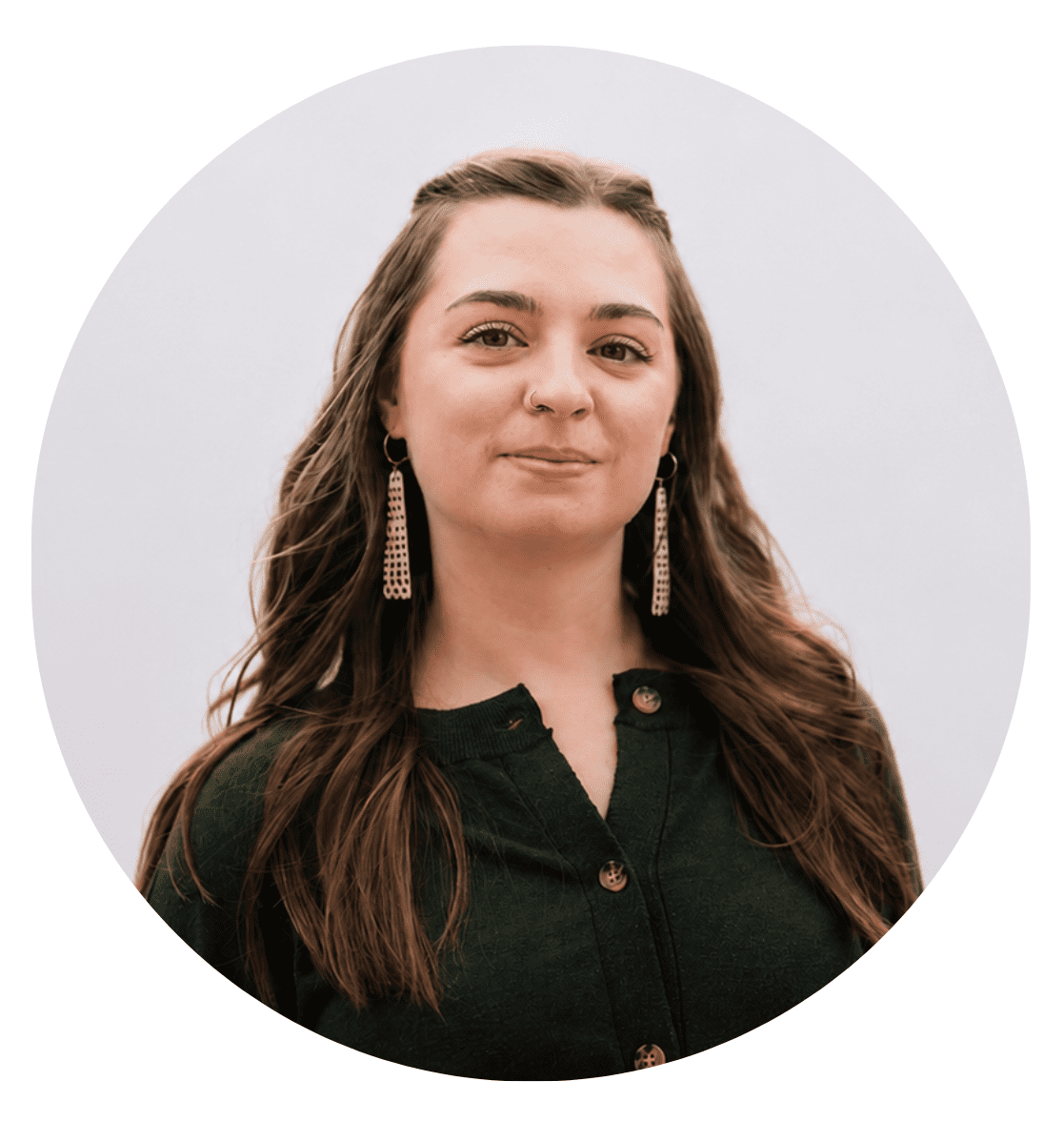 A woman with long brown hair and earrings, wearing a dark green button-up top, smiles slightly while facing the camera in front of a plain, light background—capturing the approachable spirit found in stories About RMMFI.