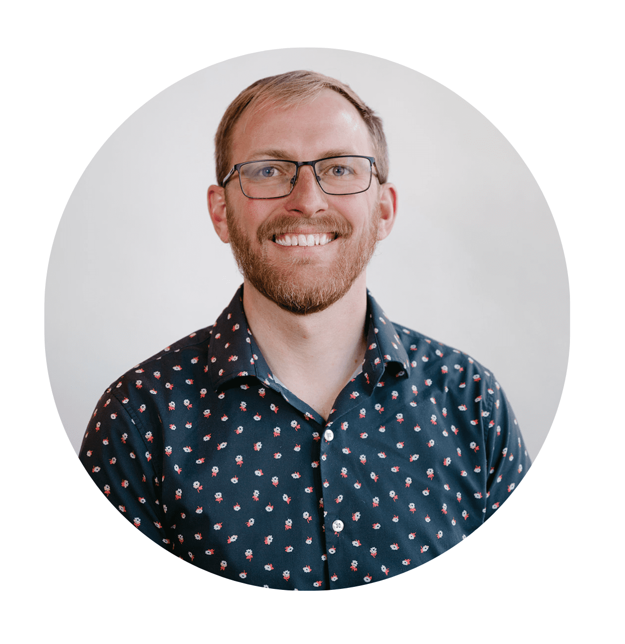A smiling man with short hair, a beard, and glasses, in a dark blue shirt with a small white and red pattern, poses in front of a plain light background—perfect for an "About RMMFI" profile introduction.