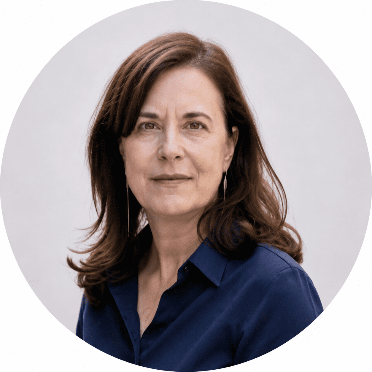 A woman with long brown hair wearing a navy blue shirt and silver earrings looks at the camera with a neutral expression, standing against a light grey background, representing the spirit of About RMMFI.