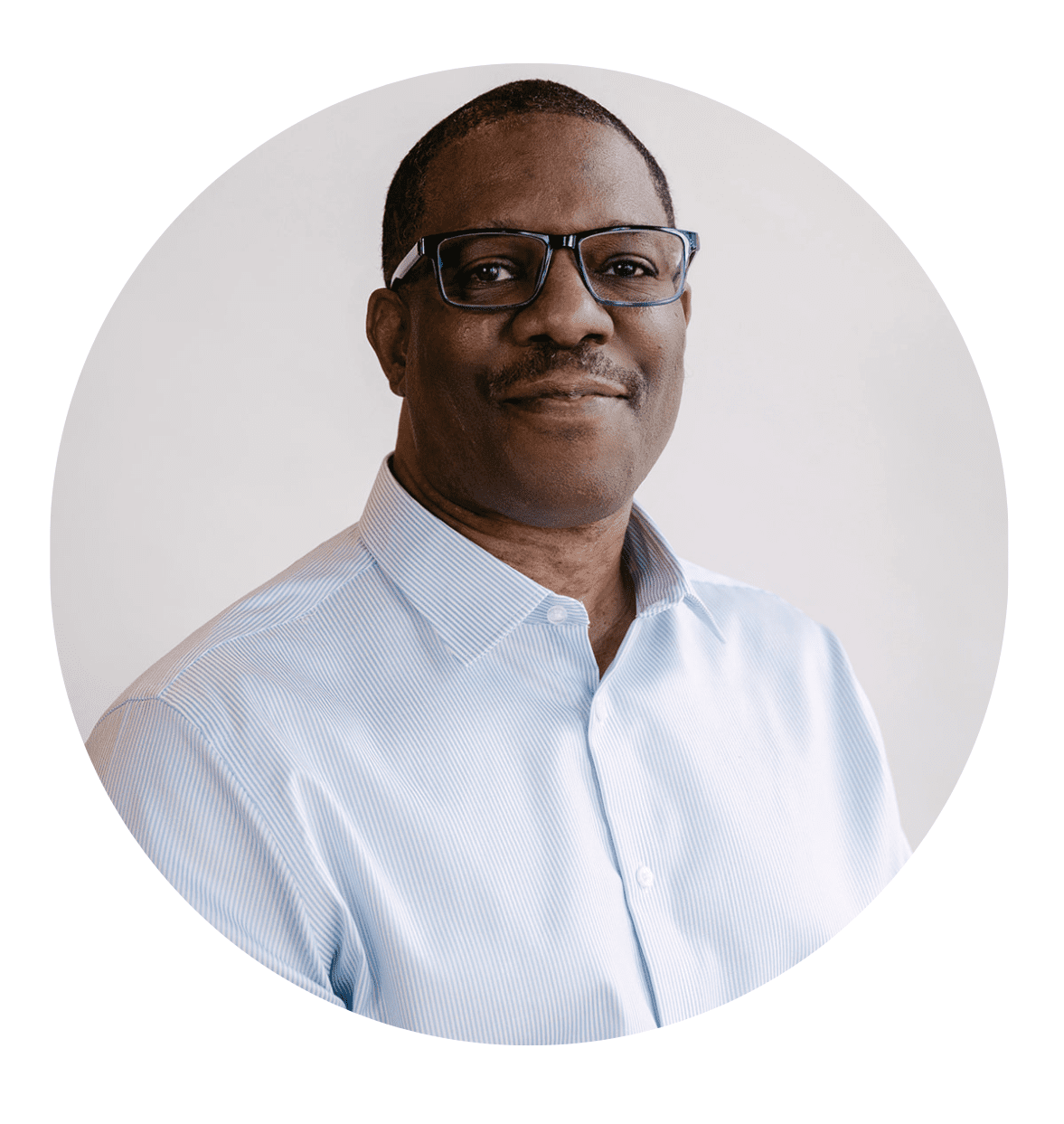 A man wearing glasses and a light blue button-up shirt is smiling slightly while facing the camera, set against a plain, light-colored background in a circular frame—an inviting image for an About RMMFI profile.
