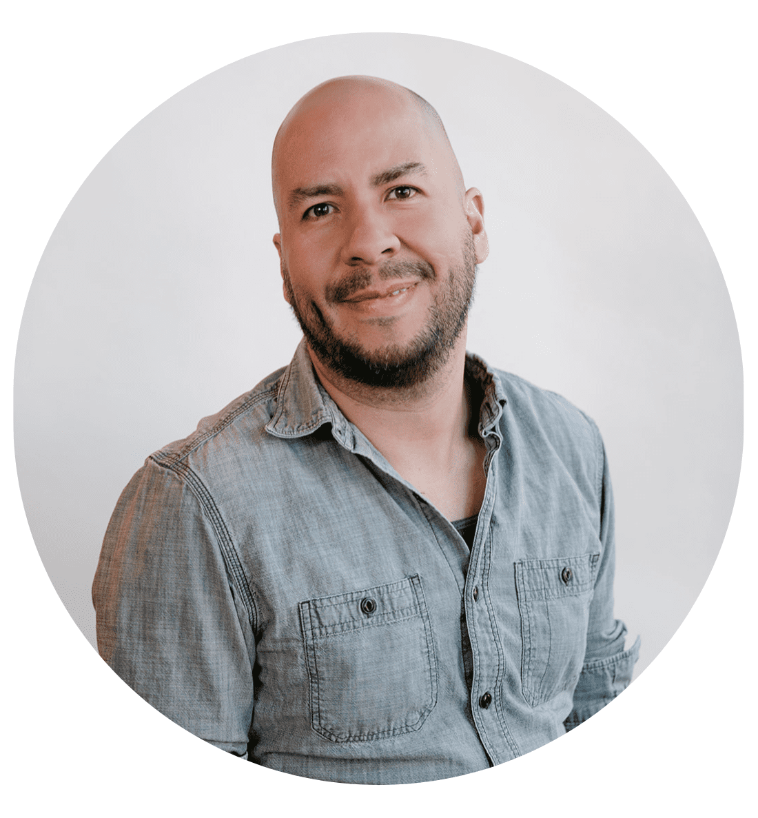 A person with a shaved head and short beard, wearing a light gray button-up shirt, smiles at the camera against a plain white background in a circular frame—perfect for an About RMMFI profile image.