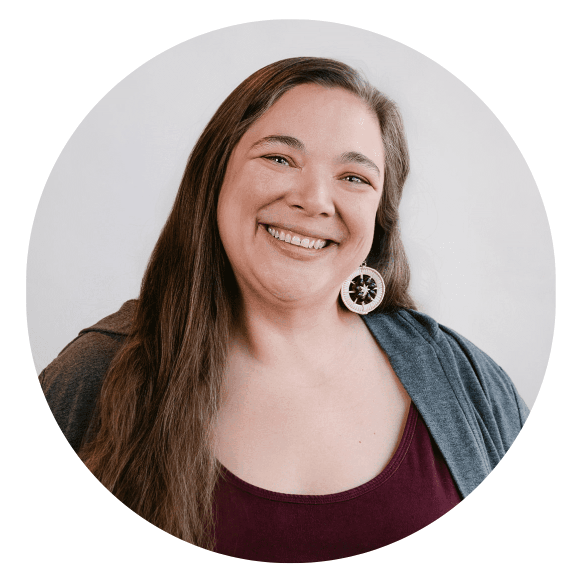 A woman with long brown hair smiles at the camera. She is wearing a maroon top, a gray cardigan, and large round earrings. The plain white background ensures the focus remains on her—perfect for an "About RMMFI" profile photo.